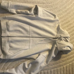 Nike Single Swoosh grey - Snygg ljusgrå hoodie från Nike med hel dragkedja, huva med snörning och två stora fickor framtill. Klassisk och clean design med liten vit Nike-logga på bröstet. Perfekt för chill dagar eller när du vill ha en enkel streetstyle-look. Storlek M (Herr) men passar garanterat L med cropped fit.