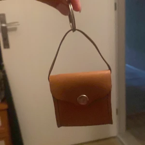 Brun miniplånbok i skinn med knapp - Söt liten plånbok i brunt äkta skinn med metallknapp och nyckelring. Perfekt för småsaker eller som accessoar till väskan. Enkel design med lock och handtag, smidig att ta med överallt. Den är även handmade och aldrig använt, helt ny. Köptes för 2-3 veckor sedan 🤗🧳💕💕