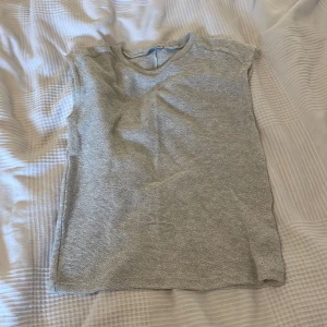 Glittrig stickad topp från Zara - Säljer en ljusgrå stickad topp från Zara med glittriga inslag. Toppen är ärmlös med rund halsringning och har en snygg, enkel design som passar perfekt till jeans eller kjol. Materialet är mjukt och skimrar snyggt i ljuset.