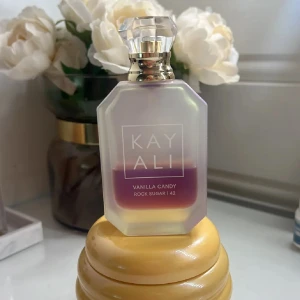 Kayali Vanilla Candy Rock Sugar 42 - Kayali Vanilla Candy Rock Sugar 42 är en parfym i en lyxig, frostad glasflaska med multifacetterad kristallkork. Doften har noter av sockrad päron, söt viol, bubbelgum, vit kola, sockerkristall och vaniljkräm. Flaskan har en lila tonad vätska och elegant design.