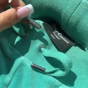Turkosa mjukisbyxor Juicy Couture XXS - Turkosa mjukisbyxor från Juicy Couture i supermjuk velour. Byxorna har snörning i midjan med silvriga detaljer, fickor både fram och bak med tryckknappar där bak.  Jätte fina och nytt skick. 