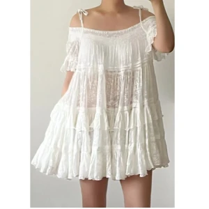 Vit volangklänning med knytband - Superfin vit kortklänning med volanger och tunna axelband som knyts på axlarna. Klänningen har offshoulder-detalj, ärmlös design och ett luftigt, flowy tyg med lätt struktur. Perfekt för varma dagar och ger en romantisk vibe.