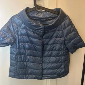 Blå kortärmad dunjacka från Herno - Snygg blå dunjacka från Herno med korta ärmar och boxig passform. Jackan har en hög krage och stängs med knappar framtill. Perfekt för lager-på-lager och ger en cool vibe till din outfit.