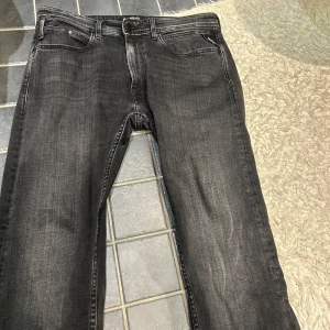Replay svarta jeans straight fit - Säljer ett par svarta jeans från Replay med klassisk femficksdesign och diskreta slitningar. Jeansen har raka ben och snygga detaljer på bakfickorna. Materialet är mjukt och stretchigt jeans, perfekt för en avslappnad stil.