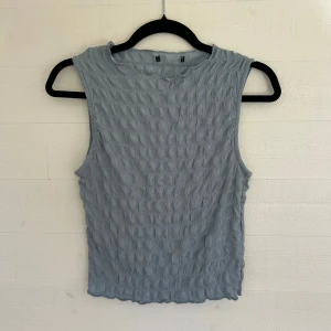 Ljusblå ärmlös linnetopp - Säljer en ljusblå ärmlös linnetopp från Gina Tricot med coolt strukturerat tyg och rund halsringning. Toppen har en lätt croppad passform och vågig kant nertill, perfekt för att lyfta din outfit med en unik touch. Lappen är bortklippt men skulle säga att den passar S🤩💕