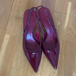Vinröda lackade pumps med spetsig tå - Snygga vinröda pumps i lackat material med spetsig tå. Storlek 37 men motsvarar storlek 38