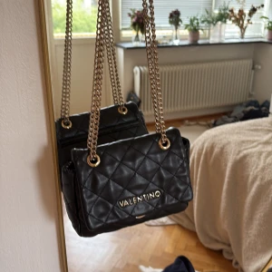 Svart quiltad axelväska från Valentino - Säljer en svart quiltad axelväska från Valentino med guldfärgade kedjor och detaljer. Väskan har ett klassiskt rutmönster och är tillverkad i skinnimitation. Perfekt storlek för det viktigaste och ger en lyxig vibe till din outfit. Köpt för 1200 priset kan diskuteras