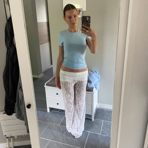 Vita spetsbyxor med låg midja - Säljer ett par vita, transparenta byxor i spets med blommigt mönster. Byxorna har låg midja och vida ben för en chill och trendig look. Perfekta att styla över bikini eller med en crop top för en cool sommarstil.