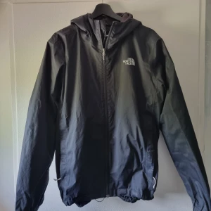 Svart vindjacka från The North Face M - Svart vindjacka från The North Face i storlek M. Jackan har huva, dragkedja framtill och logga på bröstet. Finns en liten defekt på logan framtid, 2 bokstäver saknas men jackan är fet ändå