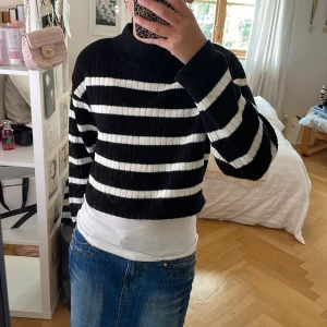Randig croppad stickad tröja H&M - Säljer en svart och vit randig croppad stickad tröja från H&M. Tröjan har ribbad struktur, hög krage och långa ärmar. Perfekt till jeans eller kjol för en chill och trendig look.