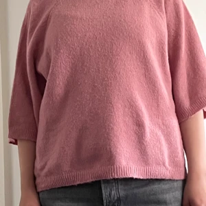 Rosa stickad tröja med trekvartsärm - Mysig rosa stickad tröja med trekvartsärmar och avslappnad passform. Tröjan har rund halsringning och ribbade kanter vid ärmslut och nederkant. Perfekt för lager-på-lager och chill dagar. Klippt bort lappen i nacken.
