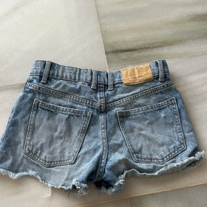 Blå jeansshorts från Zara - Säljer ett par blå jeansshorts från Zara med fransiga kanter och slitna detaljer. Storlek 10Y/140