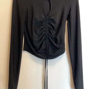 Svart långärmad topp från Amisu - Säljer en stilren svart långärmad topp från Amisu. Toppen har en snygg snörning framtill som ger en rynkad effekt och en modern look. Perfekt för att lyfta din outfit! 🖤 Den är i nyskick från new Yorker I storlek XS