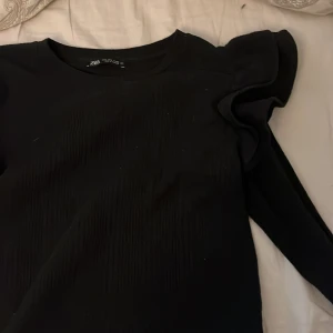 Svart tröja med volangdetaljer från Zara -  Svart tröja från Zara med volangdetaljer på axlarna o har ett ribat mönster. Den finns inte längre att köpa. storleken S💕
