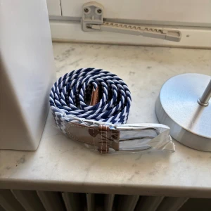 Blåvitt flätat bälte - Snyggt blåvitt flätat bälte med bruna skinninslag vid spännet. Perfekt för att ge en stilren touch till din outfit. Passar bra till både jeans och chinos.