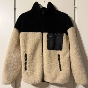 Beige och svart teddyjacka från Gina Tricot  - Säljer en teddyjacka i beige och svart med dragkedja framtill. Jackan har en praktisk bröstficka med dragkedja och två sidofickor. Använd några gånger, har tecken på användning men är i bra skick. På insidan kan man se lite noppor, samt på ena fickan på insidan är det några små fläckar. Inget som syns utanpå och går säkert bort i tvätten.
