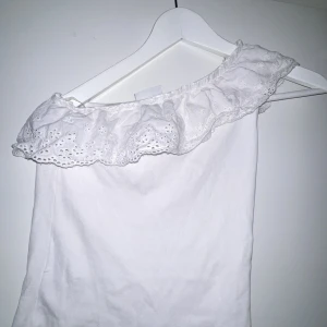 Vit offshoulder topp från Kappahl - Säljer en söt vit offshoulder topp från Kappahl med vacker spetsvolang längs kanten. Perfekt för sommarens varma dagar. Toppen har en luftig och bekväm passform.
