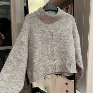 Grå stickad tröja från Gina Tricot - Säljer en mysig grå stickad tröja från Gina Tricot. Tröjan har en hög krage och är croppad med långa ärmar. Perfekt för kyliga dagar!