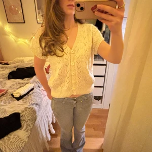 Vit stickad kofta - Säljer en söt vit stickad kofta med korta ärmar och v-ringning. Koftan har ett fint hålmönster och knappar framtill. Perfekt för lager-på-lager-stil och ger en mysig känsla. Skriv vid frågor💞💞💞