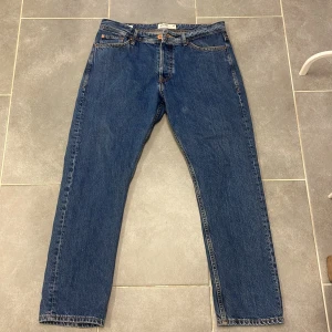  Jack and Jones jeans relaxed fit - Klassiska blå jeansbyxor från Jack and Jones  med fem fickor och knappgylf. De har en rak passform och är perfekta för en avslappnad 31-30
