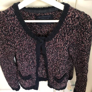 Mönstrad stickad kofta från edc - Säljer en snygg stickad kofta från edc med ett unikt mönster i svart, rött och vitt. Koftan har långa ärmar och knappar framtill. Perfekt för att hålla sig varm och stilren under kyligare dagar.