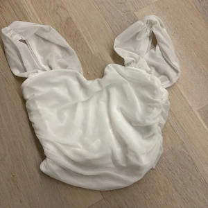 Vit ärmlös topp - Säljer en stilren vit ärmlös topp med breda söta axelband. Toppen har en elegant drapering och är tillverkad i ett lätt och luftigt material. Perfekt för varma dagar. Tröjan är väldigt kort men super fin till en kofta eller liknande:) 