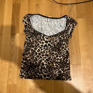 Leopardmönstrad topp med v-ringning - Snygg leopardmönstrad topp med v-ringning och korta ärmar. Perfekt för att ge en djärv touch till din outfit. Toppen har en figurnära passform och är tillverkad i ett mjukt material. För liten för mig så har inga bilder på. Aldrig använd.