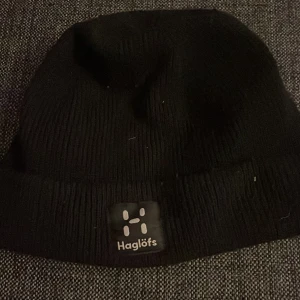 Svart mössa från Haglöfs - Snygg svart mössa från Haglöfs med ribbad design. Perfekt för kyliga dagar och enkel att matcha med olika outfits. Diskret logga framtill ger en stilren look.