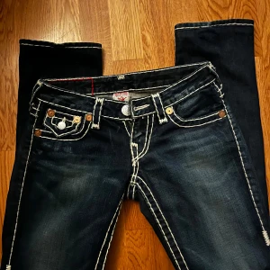 Mörkblå jeans från True Religion - Snygga mörkblå jeans från True Religion med vita sömmar och sin klassiska femficksdesign. Jeansen har en låg midja och bootcut. Perfekt skick! Skicka för mått & fler bilder🩵