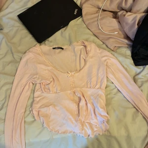 Rosa långärmad topp från Gina tricot  - Säljer en söt rosa långärmad topp från Gina tricot . Toppen har en fin spetsdetalj längs kanterna och en liten rosett framtill. Perfekt för en romantisk look. 💖