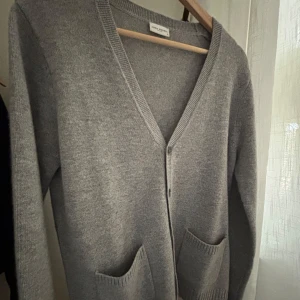 Helt ny ljusgrå kashmir cardigan från John Henric - Säljer en stilren grå kofta från John Henric i storlek S. Koftan är tillverkad i en mjuk blandning av ull och kashmir, vilket gör den både varm och bekväm. Nypris är 1299. Koftan är aldrig använd utan bara provad. Den har en v-ringad design med knappar framtill och praktiska fickor. Pris kan diskuteras vid snabb och smidig affär, kom DM för funderingar eller frågor.