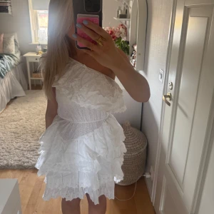 Vit oneshoulder klänning med volanger/studentklänning - Säljer en söt vit oneshoulder klänning med volanger och spetsdetaljer. Perfekt för studenten!!
