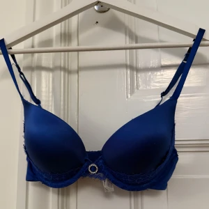 Blå bh med spetsdetaljer - Snygg blå bh med spetsdetaljer och en liten rosett framtill. Justerbara axelband för perfekt passform. Perfekt för att känna sig både bekväm och stilren.