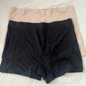 Svarta och beige under kjol 2st - Två par shorts i svart och beige. De är designade för att sitta bekvämt och har en elastisk midja. Perfekta för att bäras under klänningar eller kjolar för extra komfort.