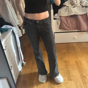 Svarta jeans med bootcut - Snygga svarta jeans med bootcut-stil och låg midja. De har klassiska femficksdetaljer och knappar i silverfärg. 