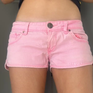 Rosa jeansshorts LOW WAISTED - Snygga rosa jeansshorts med låg midja och klassisk femficksdesign. Perfekta för varma sommardagar. De har en knapp och dragkedja framtill för enkel stängning.