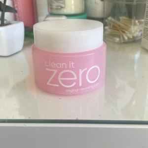 Clean It Zero Original Cleansing Balm - Säljer en rosa burk med Clean It Zero Original Cleansing Balm från Banila Co. Denna rengöringsbalm är perfekt för att ta bort smink och orenheter. Burken har en vit skruvlock och innehållet är en mjuk balm som smälter vid kontakt med huden.