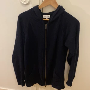 Mörkblå  hoodie från Davida - Säljer en stilren mörkblå hoodie från Davida med dragkedja framtill. Tröjan har långa ärmar och en bekväm huva, perfekt för kyliga dagar. Passar både till vardags och mer avslappnade tillfällen.