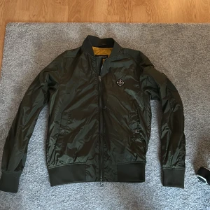 J Lindberg Jacka! - Snygg grön jacka från J Lindeberg med dragkedja och ribbade muddar. Jackan har en klassisk look med en liten logotyp på bröstet och en kontrasterande gul insida. Perfekt för en cool och avslappnad look. Köpte jackan på J.Lindeberg för 2500. Har knappt använt den!
