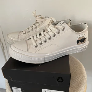 Vita sneakers från Karl Lagerfeld - Snygga vita sneakers från Karl Lagerfeld med ikonisk logga på hälen. Skorna har klassisk snörning och en stilren design som passar perfekt till vardags. De är tillverkade i syntetmaterial och har en bekväm passform. Använda 1 gång, säljes pga fel storlek