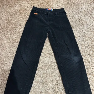 Svarta manchesterbyxor från Empyre - Snygga svarta manchesterbyxor från Empyre med en cool broderad logga. Byxorna har en klassisk design med knapp och dragkedja framtill. Perfekta för en stilren look.