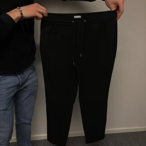 Svarta byxor från Lindbergh - Svarta byxor från Lindbergh med relaxed fit. Byxorna har en dragsko i midjan för justerbar passform. Perfekta för en avslappnad stil.