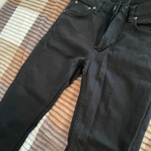 Svarta jeans från Nudie Jeans - Snygga svarta jeans från Nudie Jeans med klassisk femficksdesign. De har en dragkedja och knappar i gylfen. Perfekta för en stilren look. Använd lite 