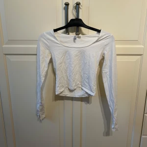 Vit croppad långärmad topp från H&M Divided - Säljer en enkel och stilren vit croppad topp från H&M Divided. Toppen har långa ärmar och en rundad halsringning. I strl S