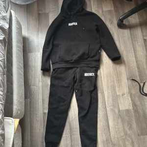 Svart set från Hoodrich - Svarta mjukisbyxor och hoddie från Hoodrich med vit logga tryck. Byxorna och hoddien har flera gömda dragkedja och är tillverkade i mjukt material, perfekta för en avslappnad stil. Storleken är lite upp och ner men den passar långa xs-s-medium