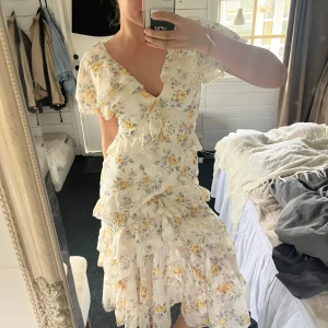 Blommig volangklänning från Boohoo - Superfin långklänning från Boohoo med blommigt mönster i ljusa färger. Klänningen har volanger, v-ringning och korta ärmar. Perfekt för sommarens alla tillfällen!