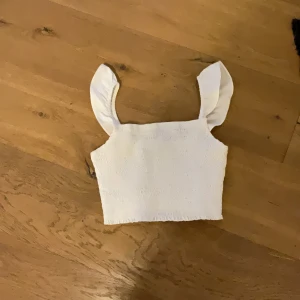 Vit croppad linnetopp med breda axelband - Säljer en söt vit croppad linnetopp med breda axelband. Toppen har en fyrkantig halsringning och är perfekt för varma dagar. Enkel och stilren design som passar till mycket.