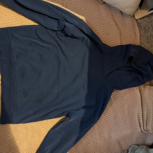 Mörkblå hoodie från Lindex - Säljer en enkel och stilren mörkblå hoodie från Lindex i storlek 158/164. Tröjan har en klassisk huva och en stor magficka framtill. Perfekt för dig som gillar en avslappnad och bekväm stil.