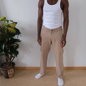 Beiga chinos med bälte - Snygga beiga chinos med normal passform och raka ben. Byxorna har klassisk design med knäppning och dragkedja samt medföljande svart bälte med spänne. Perfekta för en clean och stilren look. Atlant beige chinos  33/34.  Fits 31/30  Waist:42cm Outseam:98cm Leg-opening:21cm   Feel free to ask any questions