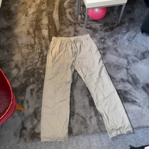 Beiga byxor med resårmidja - Säljer ett par beiga byxor med resår i midjan. Byxorna har raka ben och är tillverkade i ett lätt och mjukt material, perfekta för en avslappnad stil. Passar dig som gillar enkel och bekväm design.